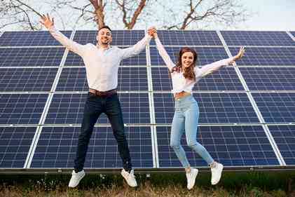 a happy young couple jumping in front of their off grid solar energy system